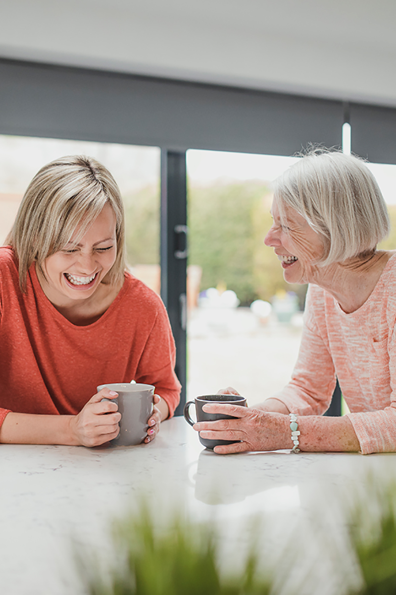 Happy mom and adult daughter laughing over tea