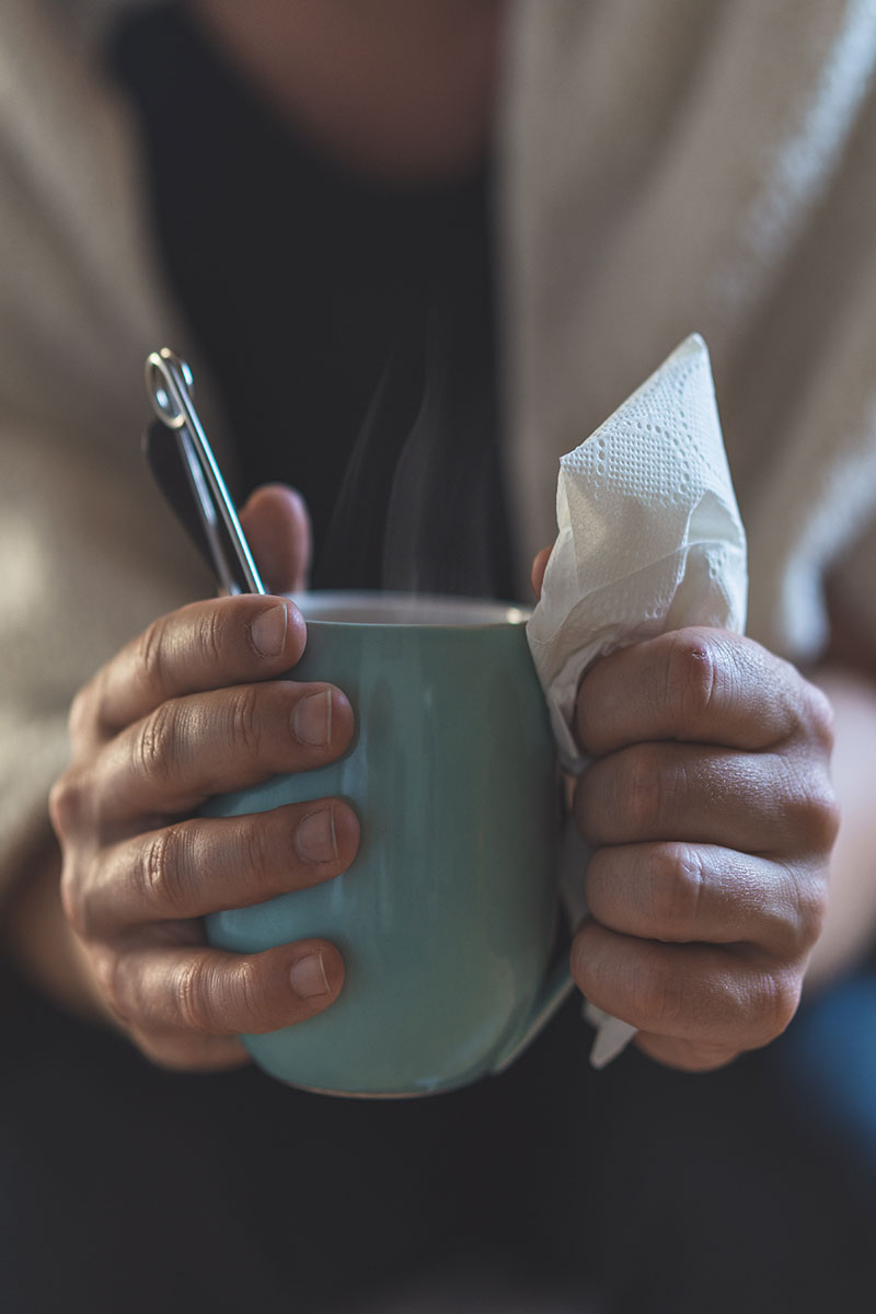 Sick woman holding cup of tea and tissues