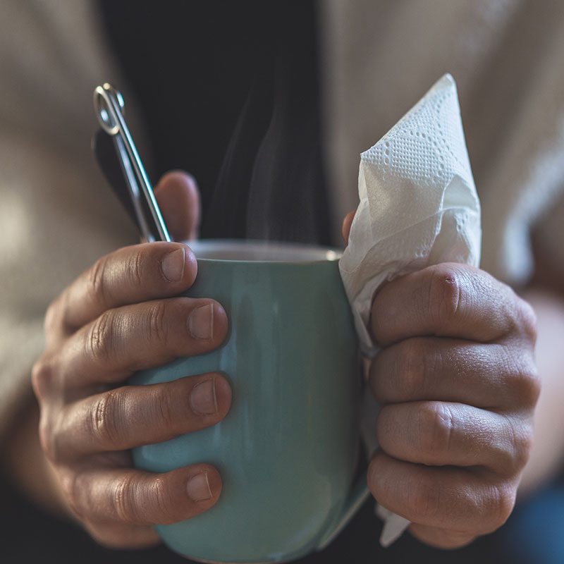 Sick woman holding cup of tea and tissues